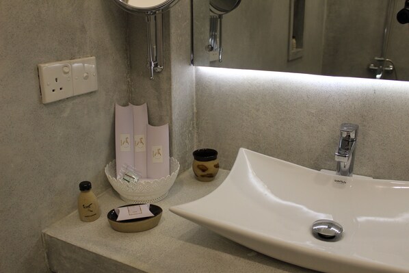 Une salle de bain avec un lavabo blanc, un miroir, un distributeur de savon et un petit bol décoratif.