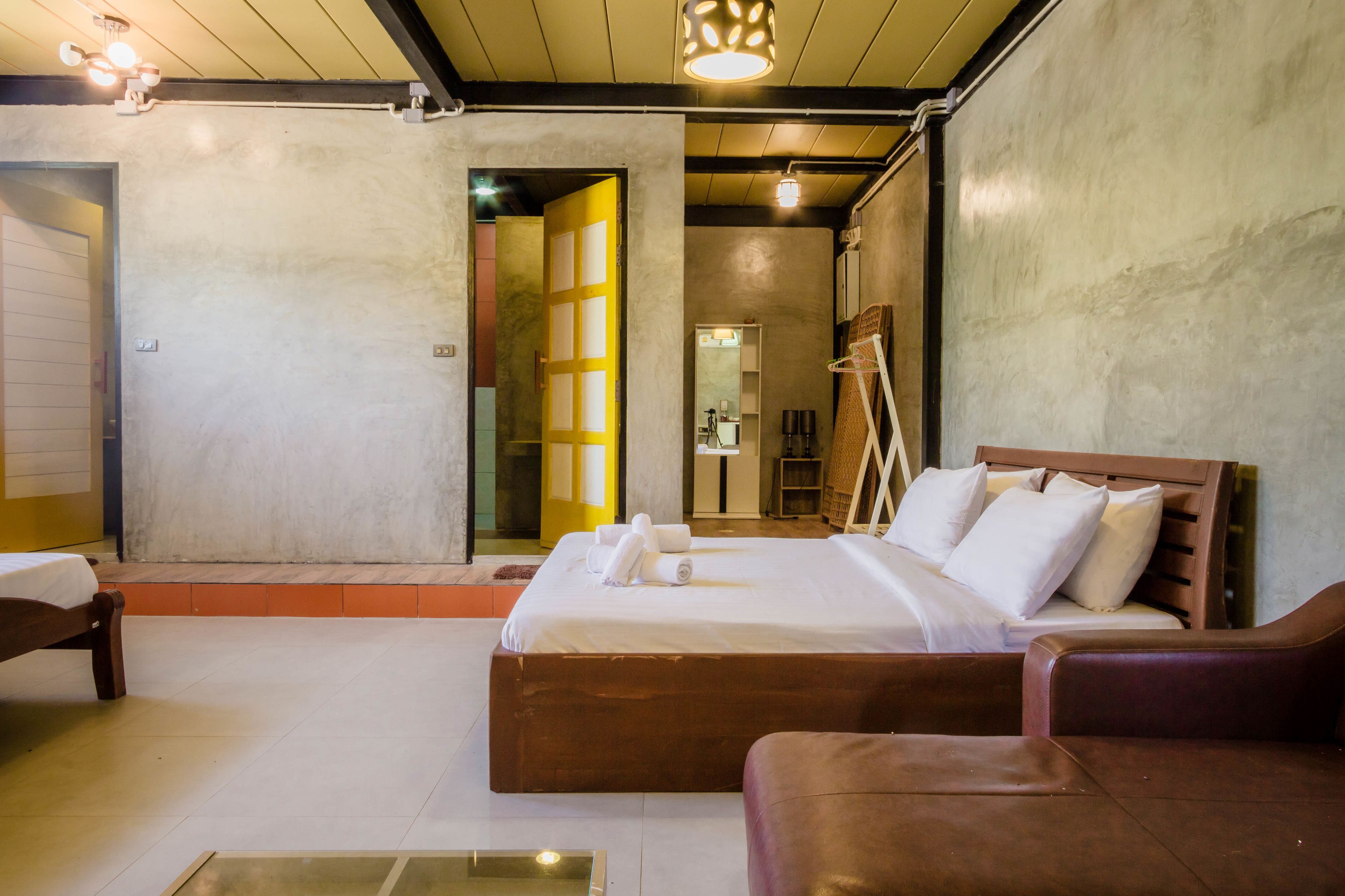 A bedroom with a large bed, a wooden headboard, and a brown leather sofa.