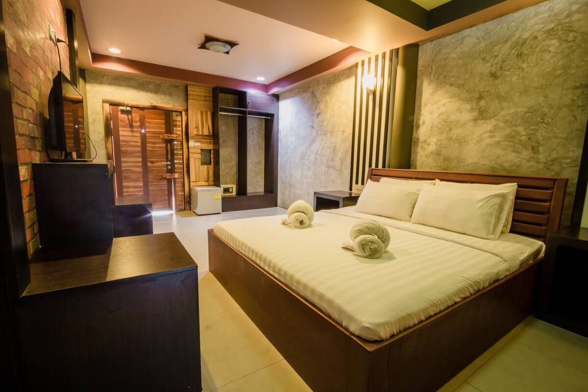 A hotel room with a large bed, a wooden headboard, a bedside table, a mirror, and a wardrobe.