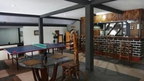 Une pièce équipée d’une table de ping-pong, d’une chaise en bois et d’un coin bar avec des tabourets.