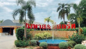 A hotel entrance with a sign in a foreign language, surrounded by tropical plants and a small fountain. - Bypass and Resort (Kanchanaburi)