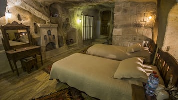 A rustic stone room with two beds, a wooden dresser, a mirror, and a stone fireplace.