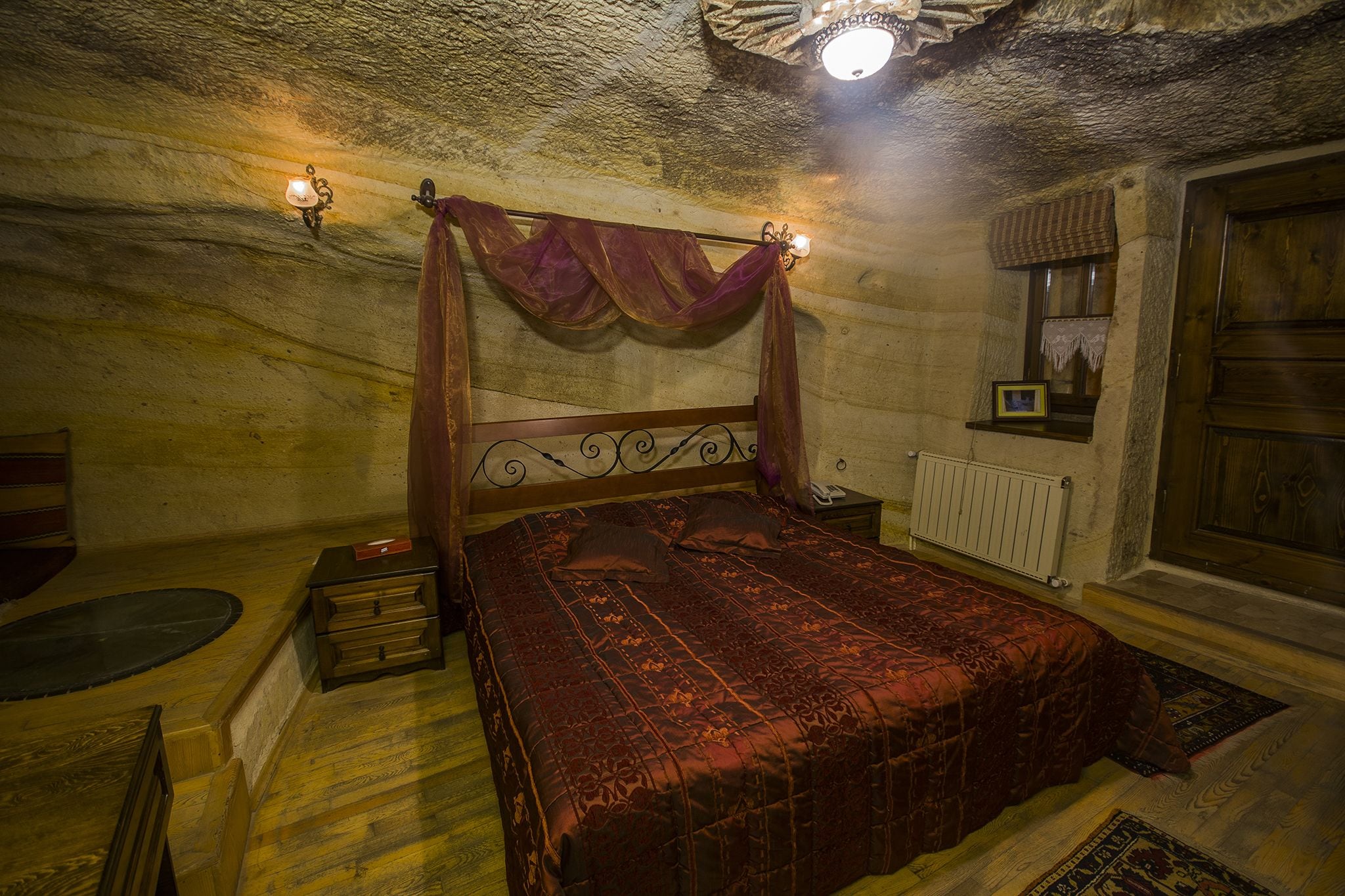 Un dormitorio con una cama de madera, una mesita de noche, una lámpara de pared y una ventana con cortina.