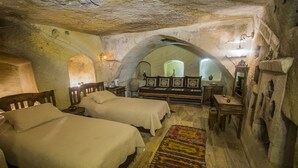 Quarto com duas camas, uma escrivaninha de madeira e paredes de pedra.
