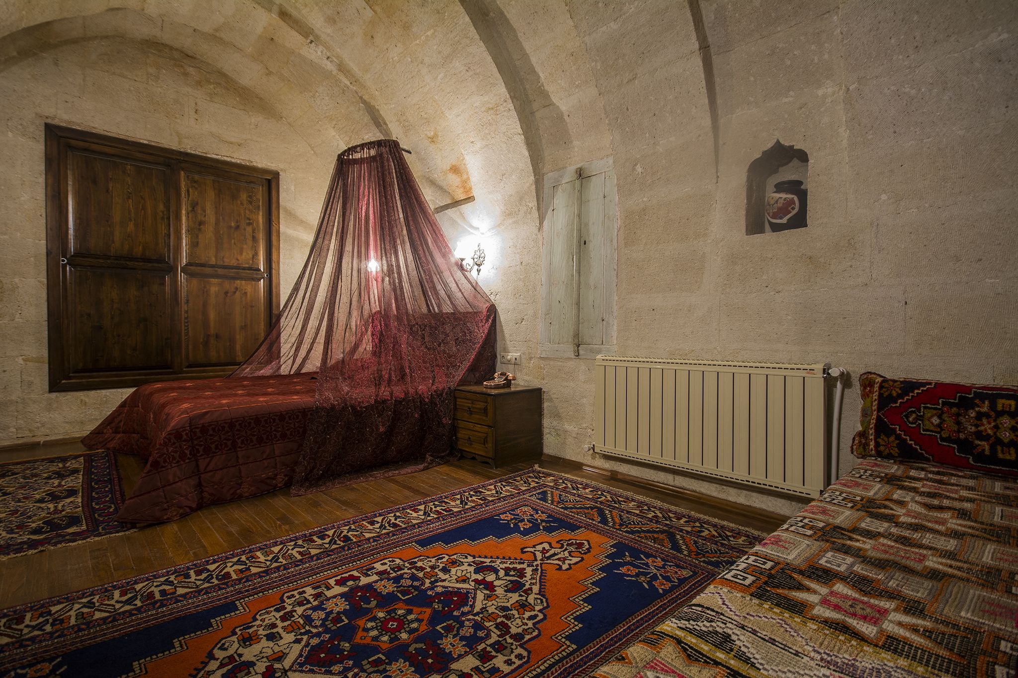 A room with a bed, a wooden wardrobe, a nightstand, a radiator, and a window with a curtain.