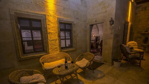 Uma área de estar acolhedora ao ar livre, com móveis de vime e uma mesa, com duas janelas e cortinas estampadas.