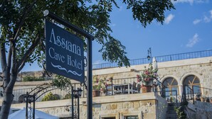 Placa do Hotel Assitana Cave com arquitetura em pedra e uma varanda com plantas em vasos.