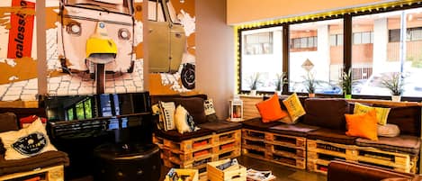 A cozy lounge area with a vintage car mural, wooden crates as seating, and a large window offering a view of the street.