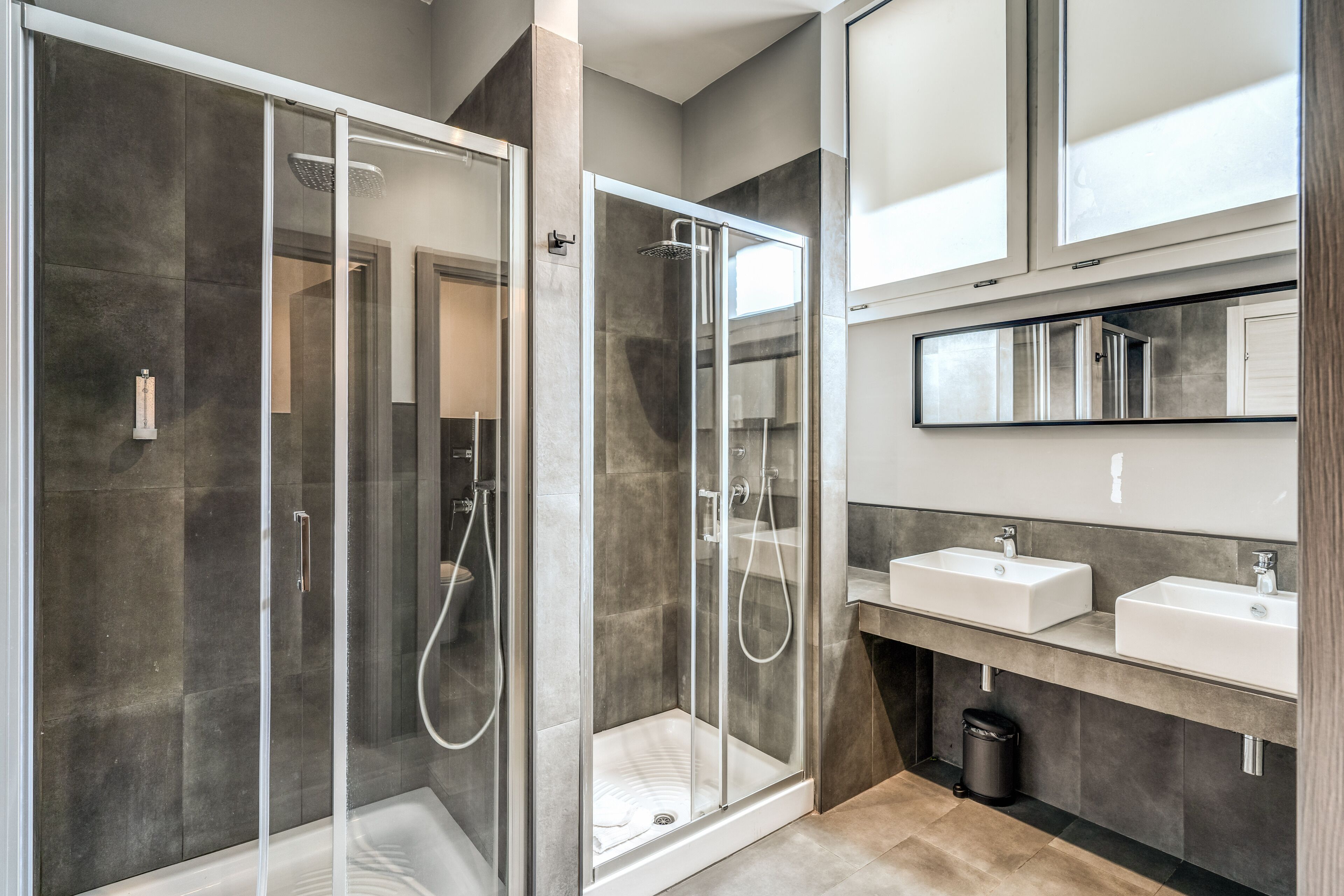 Un bagno moderno con cabina doccia in vetro, due lavabi e un grande specchio sopra il mobile.