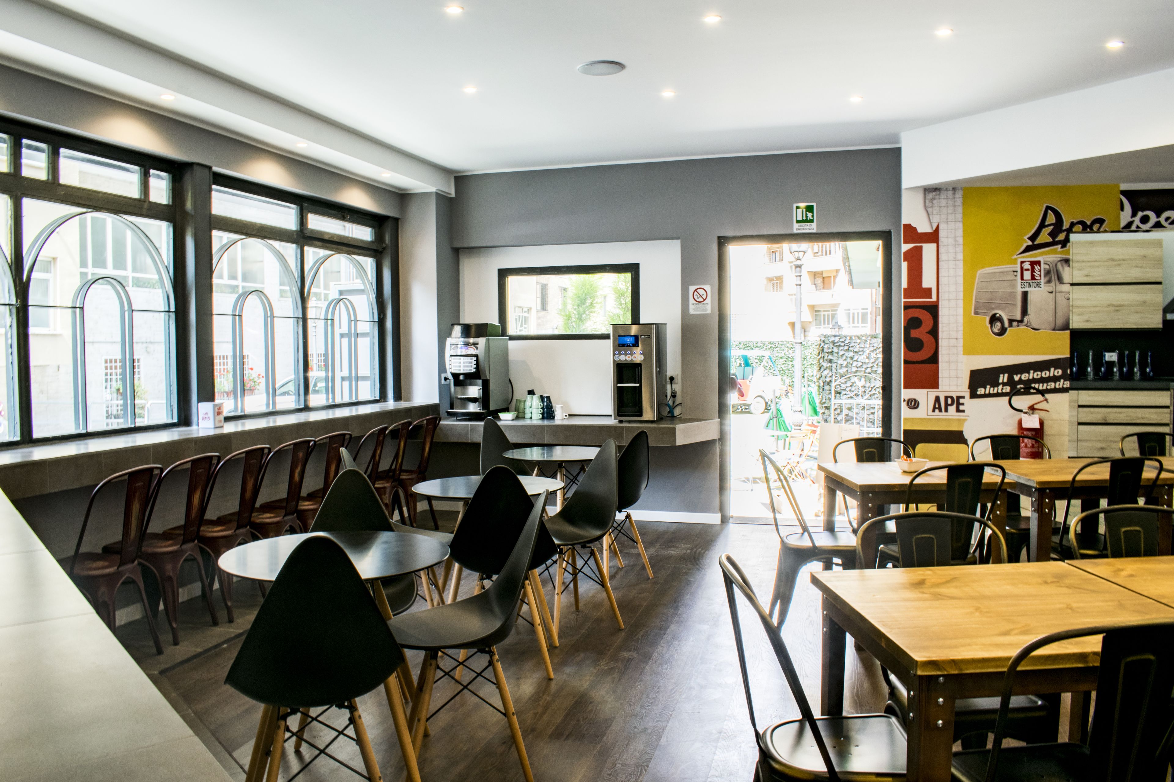 A modern cafe with round tables and black chairs, large windows, and a counter with a coffee machine.