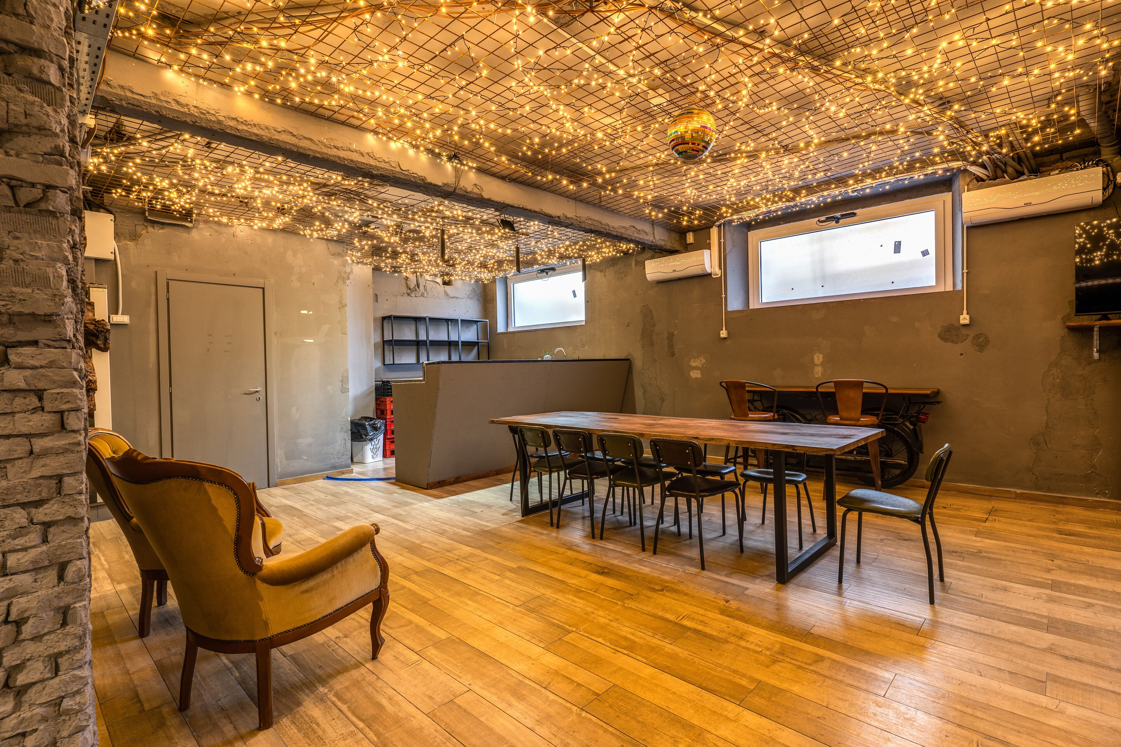 A dining area with a wooden table and chairs, a brick wall, and a ceiling adorned with string lights.