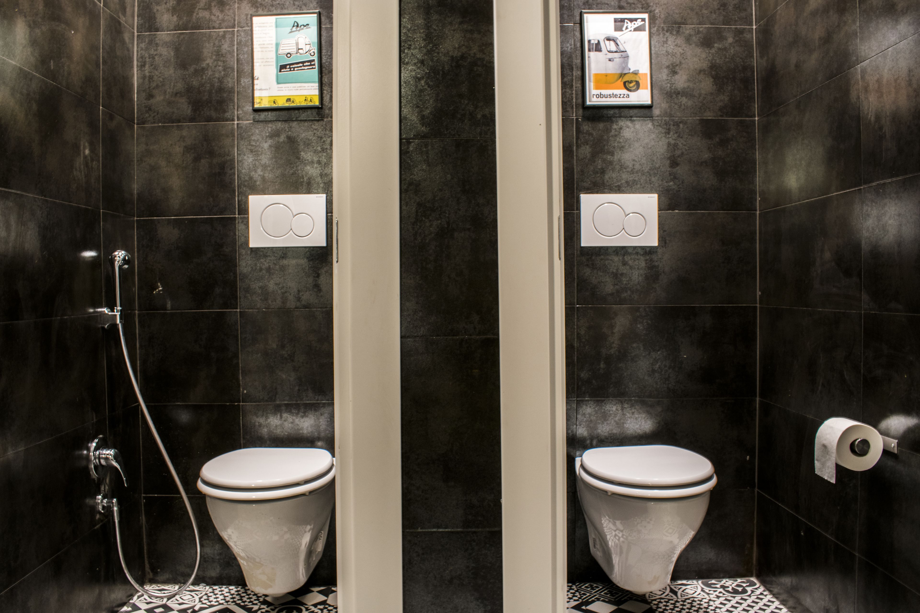 A modern bathroom with two toilets, a shower, and a toilet paper dispenser.