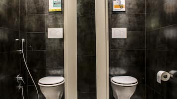 A modern bathroom with two toilets, a shower, and a toilet paper dispenser.