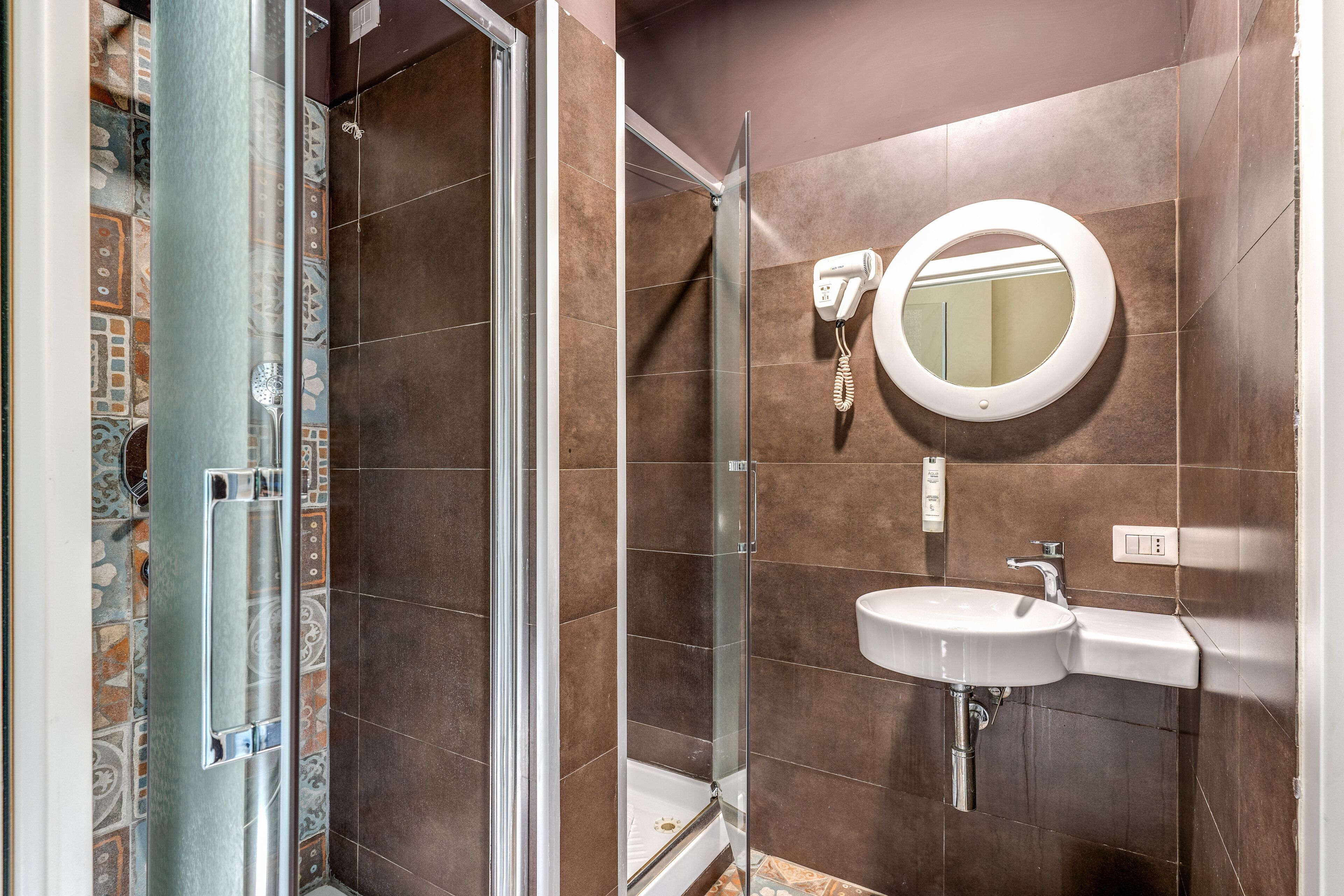 A bathroom with a glass shower enclosure, a white sink, and a round mirror.