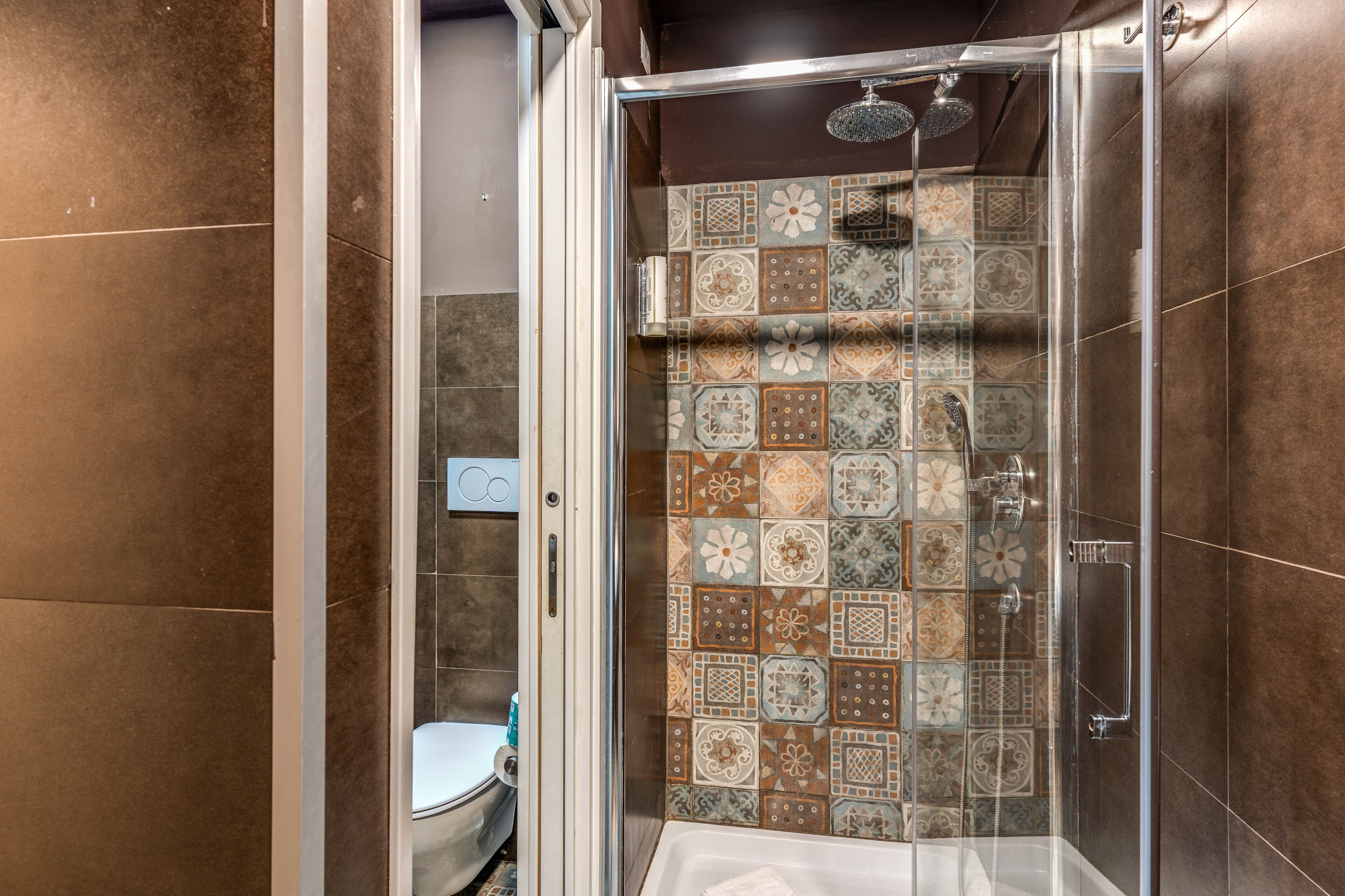 A shower with a glass door and a tiled wall.