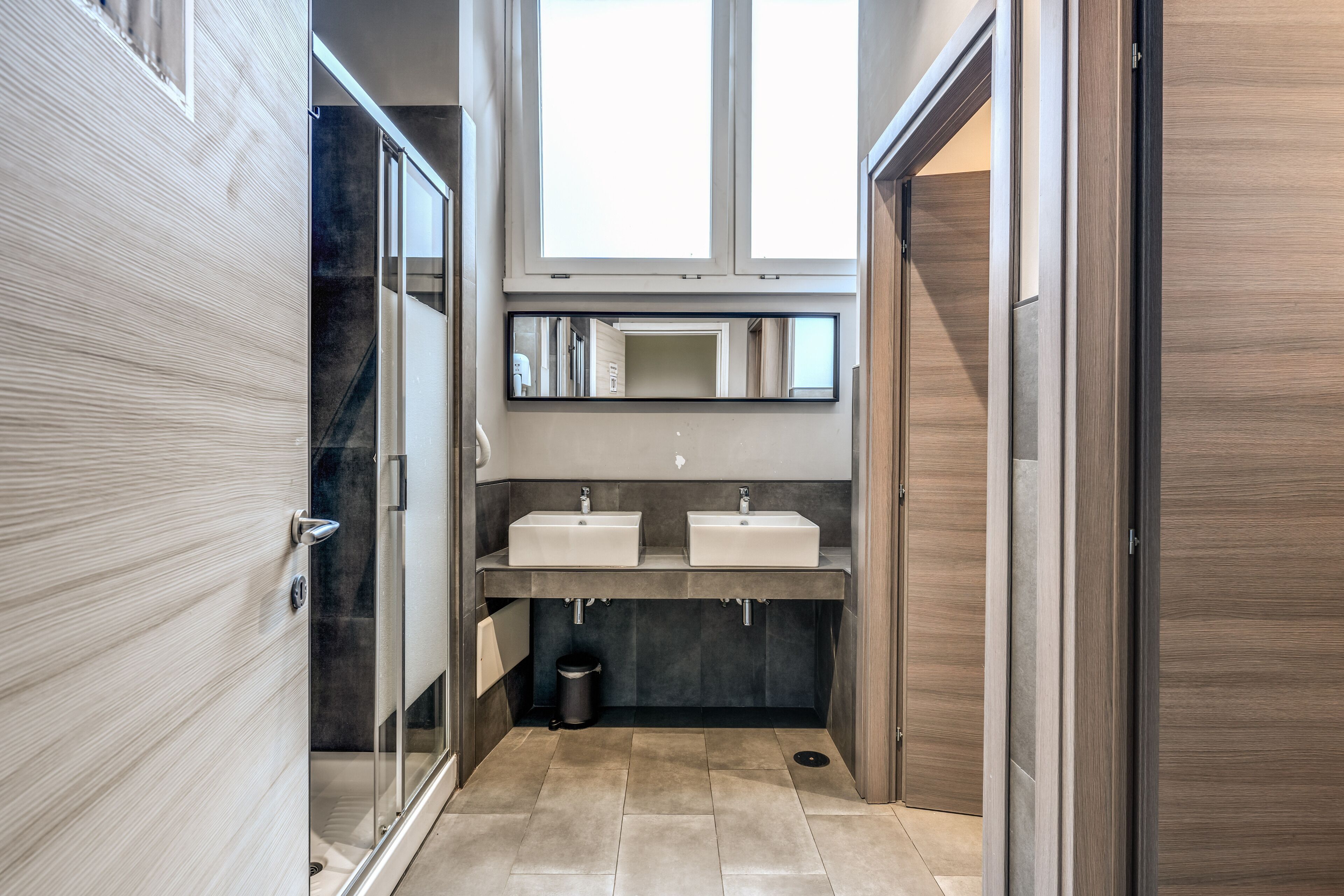 A modern bathroom with two sinks, a mirror above, and a glass shower enclosure.