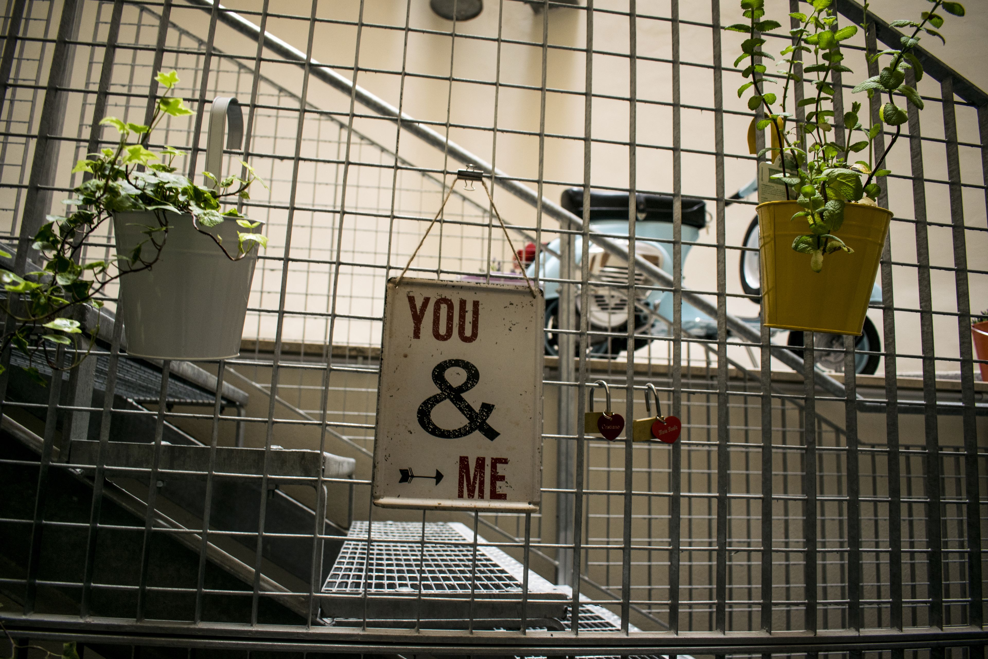 Une cage en métal sur laquelle est accrochée une pancarte indiquant « TOI ET MOI », ainsi que deux plantes en pot.