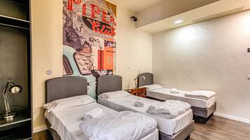 Habitación de hotel con tres camas, un escritorio con lámpara y un cartel grande en la pared.
