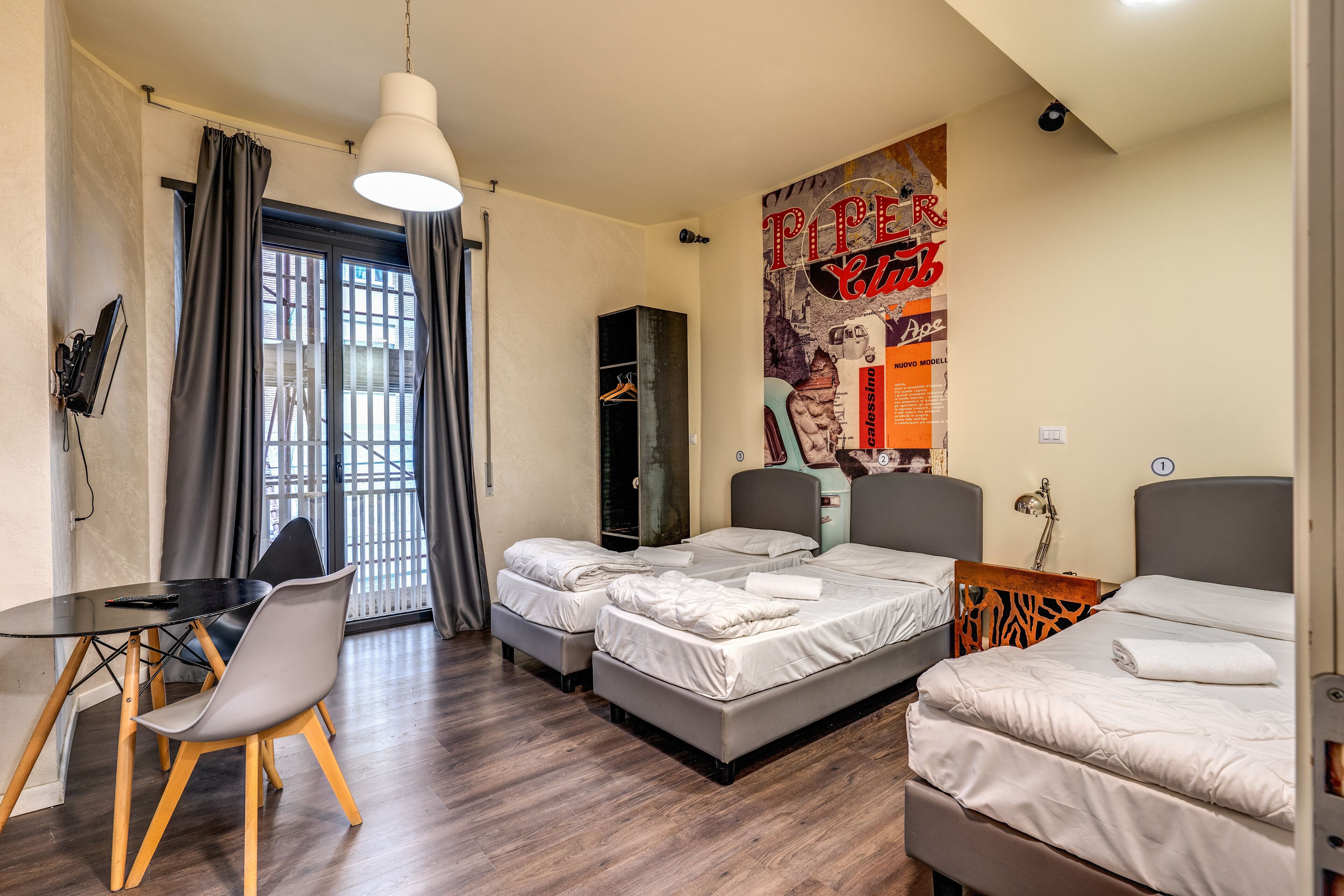 Habitació d'hotel amb dos llits, un escriptori amb cadira, una taula de dinar i un cartell gran a la paret.