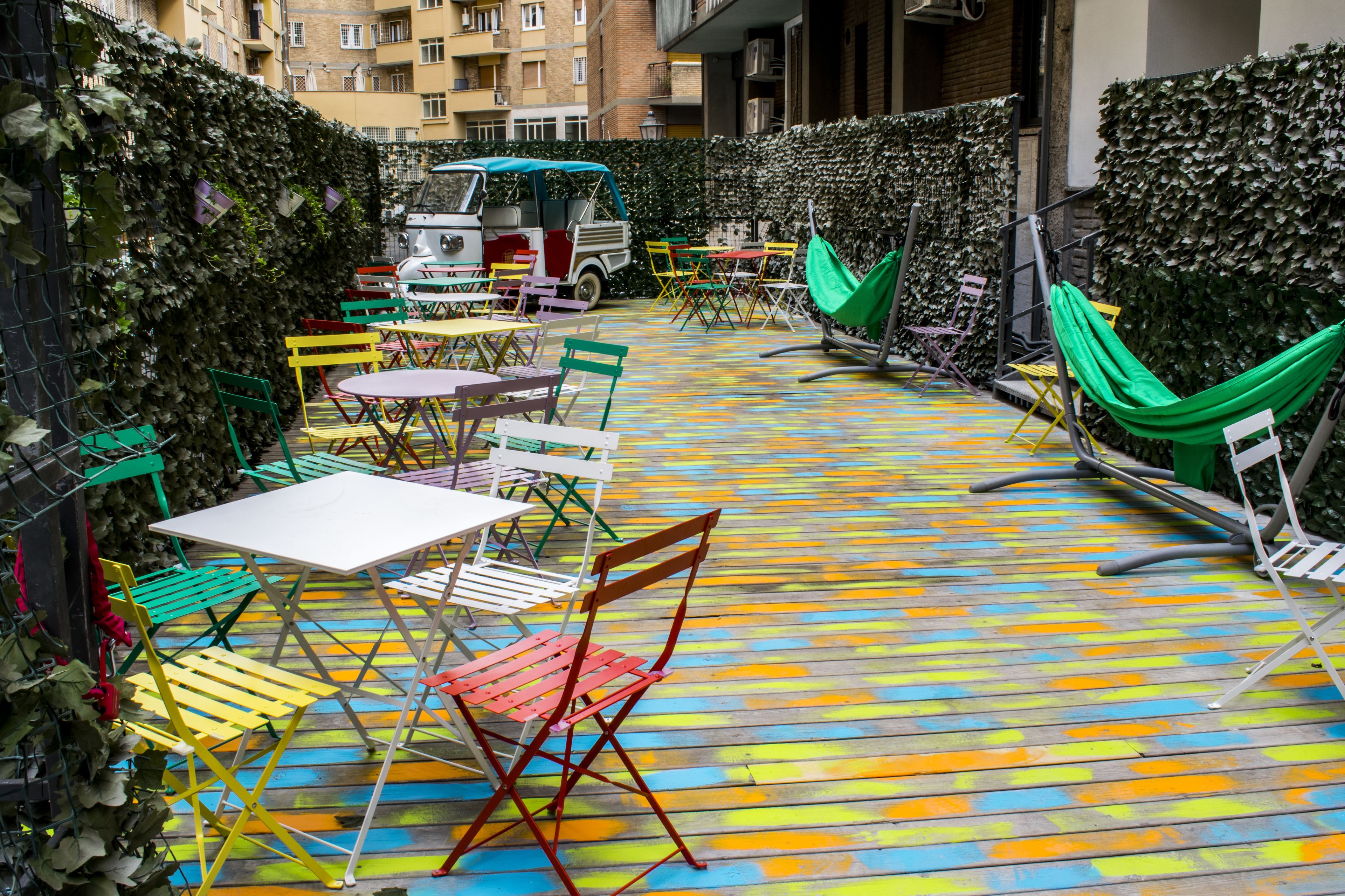 An outdoor patio with colorful wooden flooring, tables, chairs, and a green hammock.