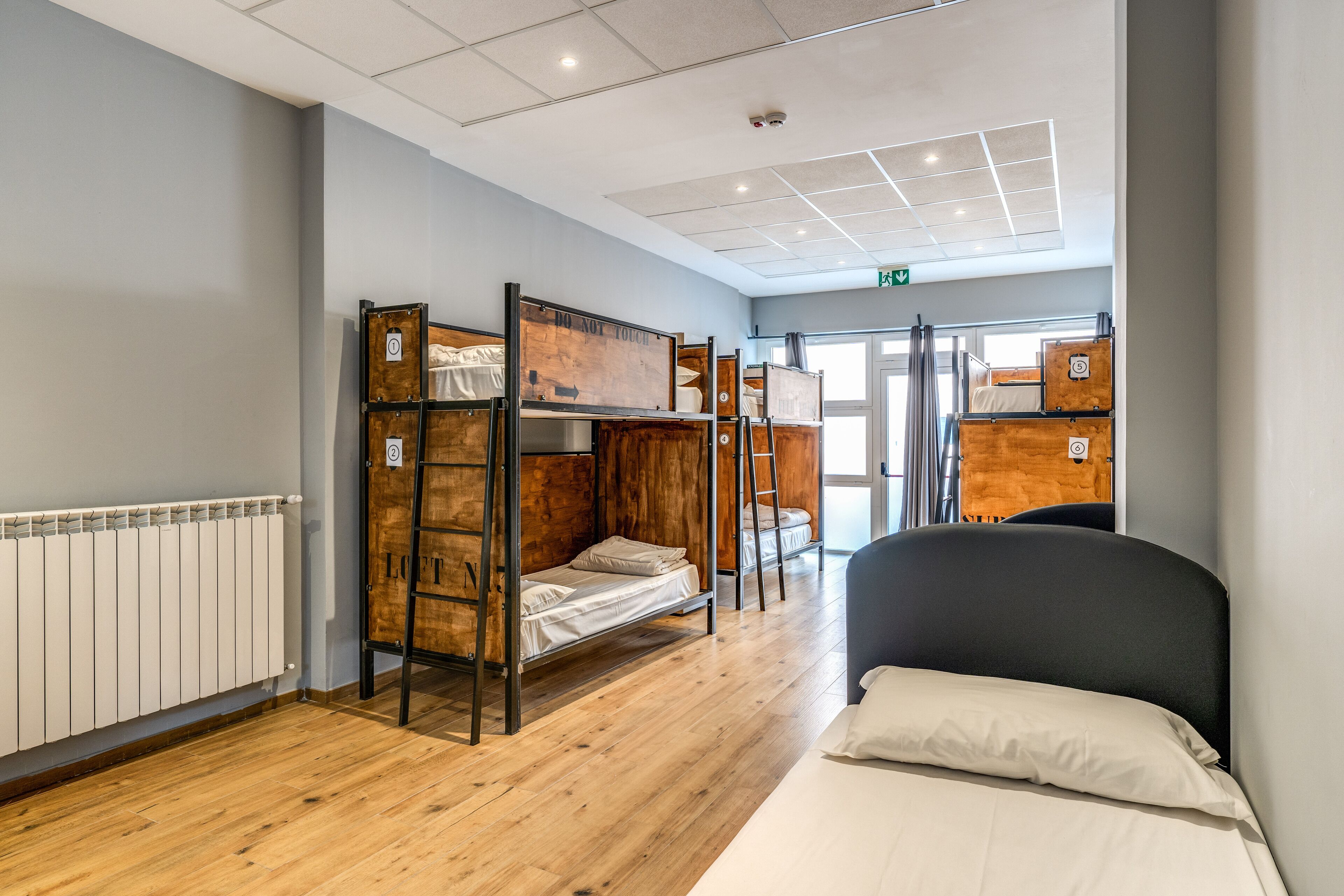 A dormitory room with bunk beds, a radiator, and a large window.