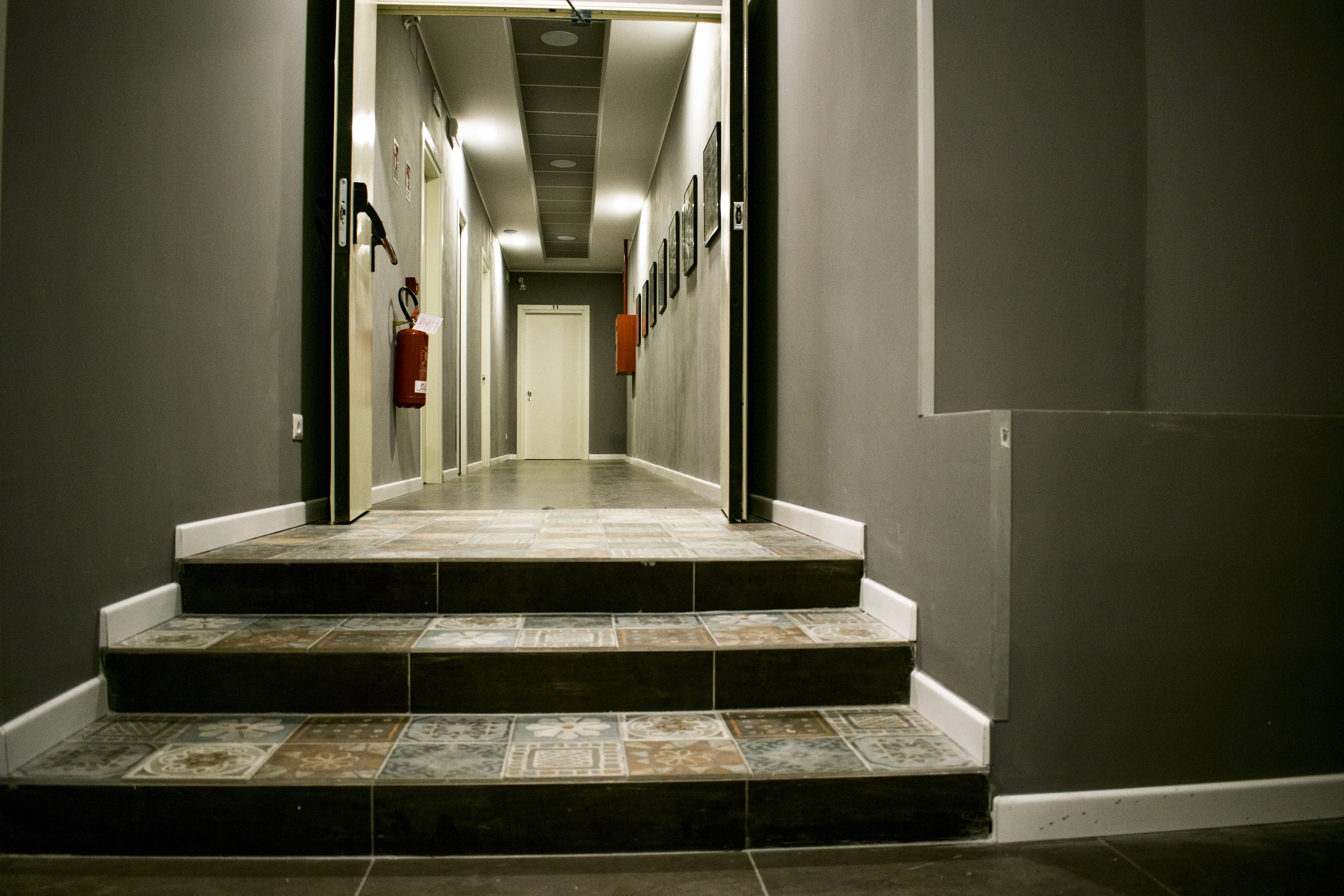 A hallway with steps leading to a door, a fire extinguisher on the wall, and a ceiling with recessed lighting.