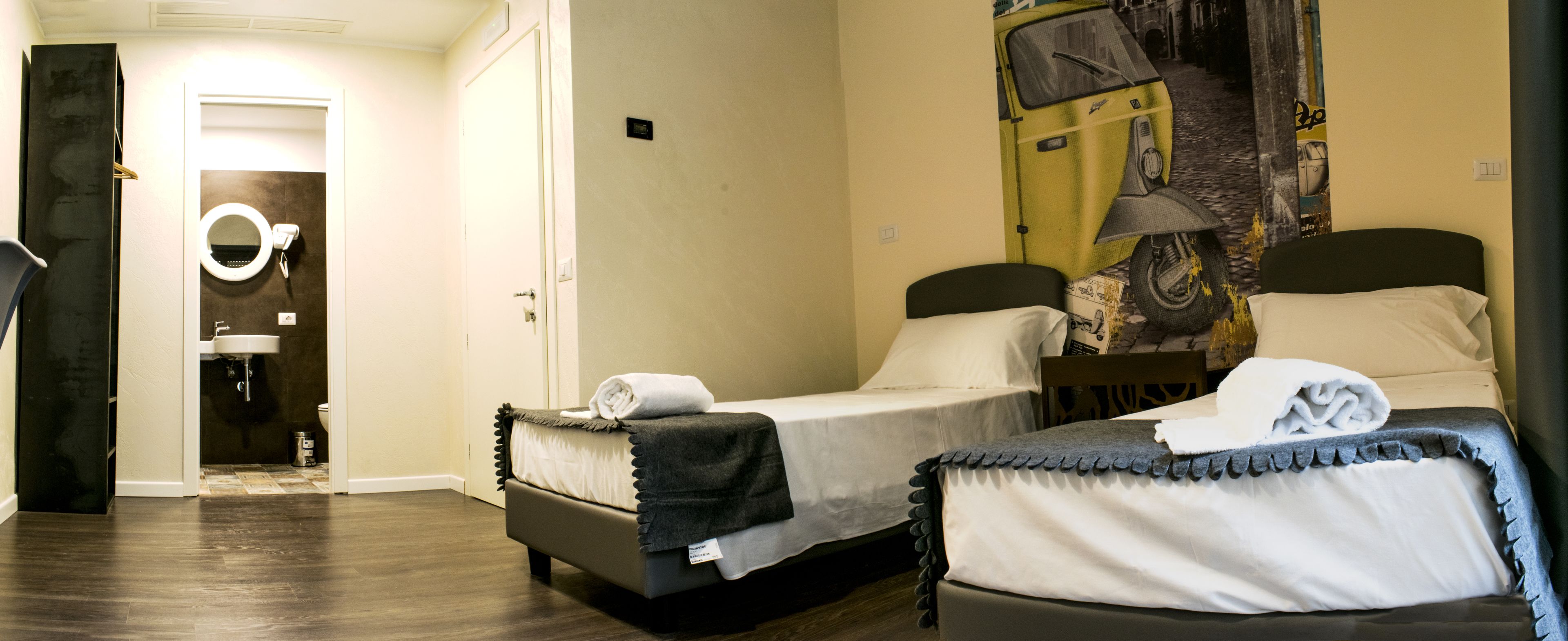 A hotel room with two beds, a bathroom with a mirror, and a mural on the wall.