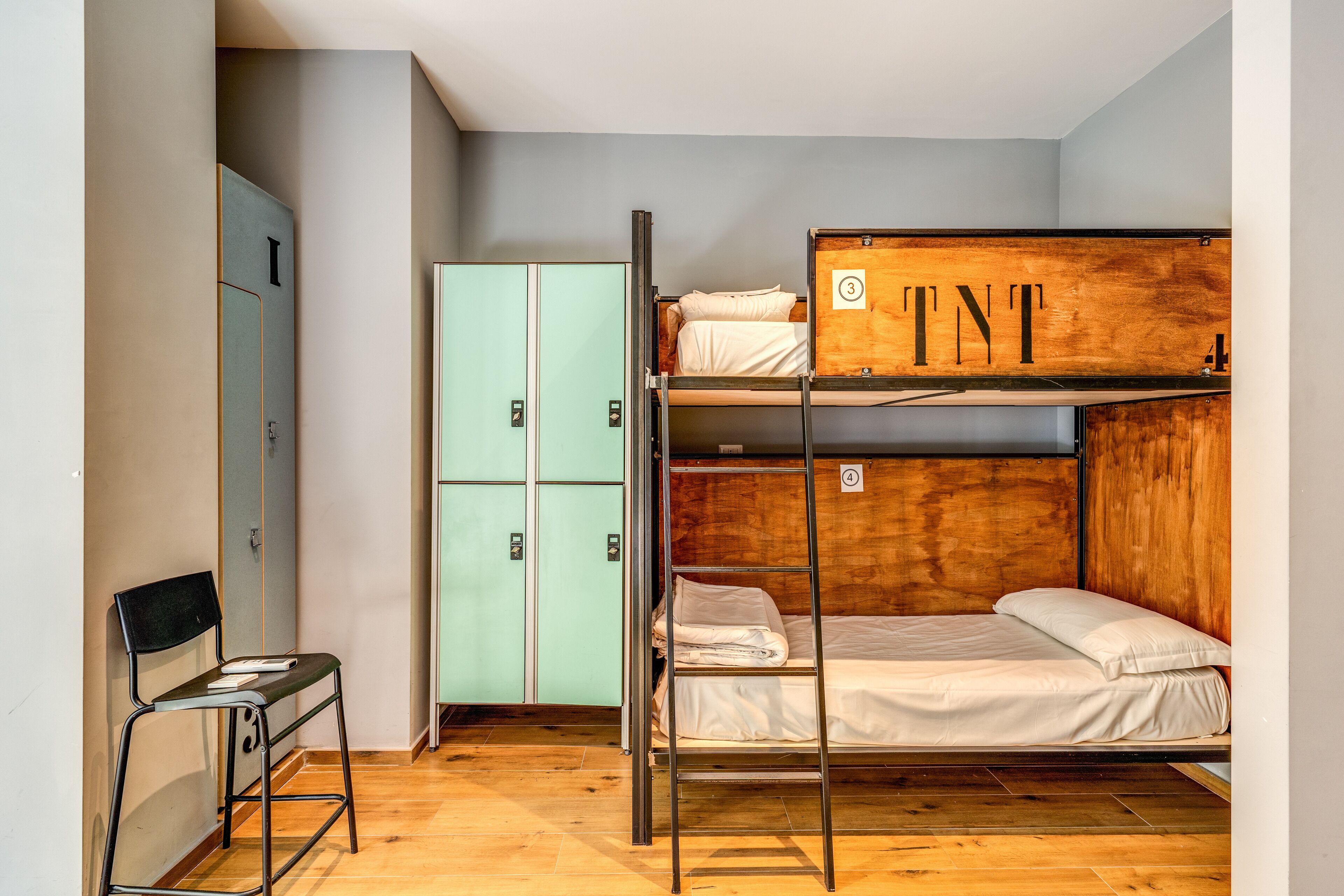Un lit superposé avec une tête de lit en bois portant l’inscription « TNT », une armoire verte et une chaise.