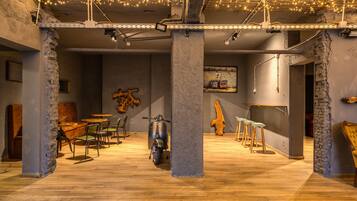 L’intérieur présente des murs en briques apparentes, un plancher en bois et un scooter. On y trouve des tables et des chaises, ainsi que des guirlandes lumineuses suspendues au plafond.