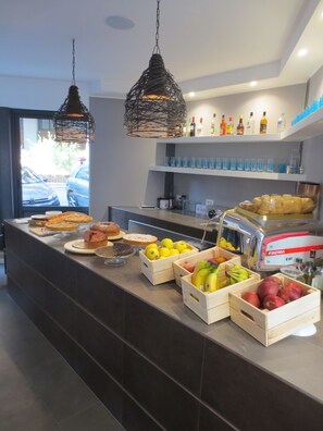 Un banco buffet con diversi alimenti, tra cui frutta e dolci, e un frigorifero con bevande.