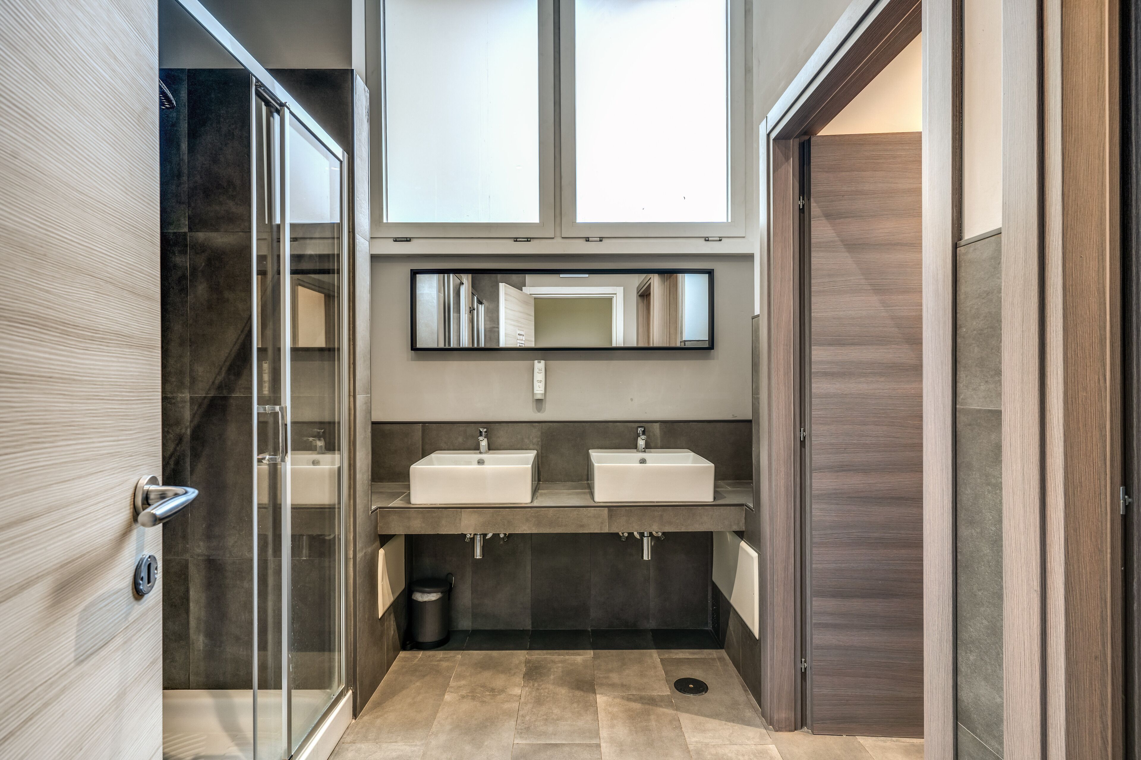 Un baño moderno con dos lavamanos, un espejo grande y una cabina de ducha de vidrio.