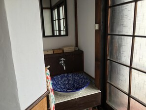 A bathroom with a blue ceramic sink, a mirror, and a window with a metal grid pattern. - Guesthouse Kiten - Hostel (Gifu)