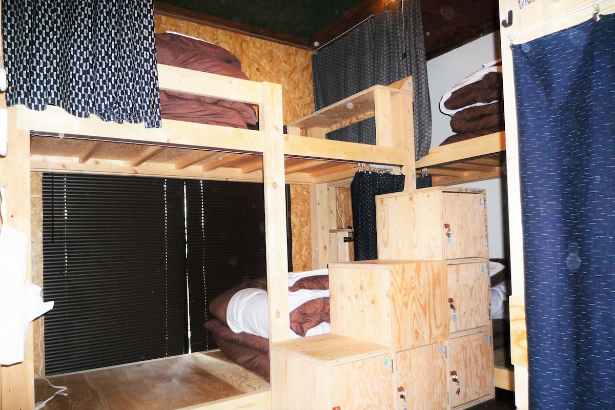 A bunk bed room with a wooden floor, a window with blinds, and a wardrobe with multiple compartments.