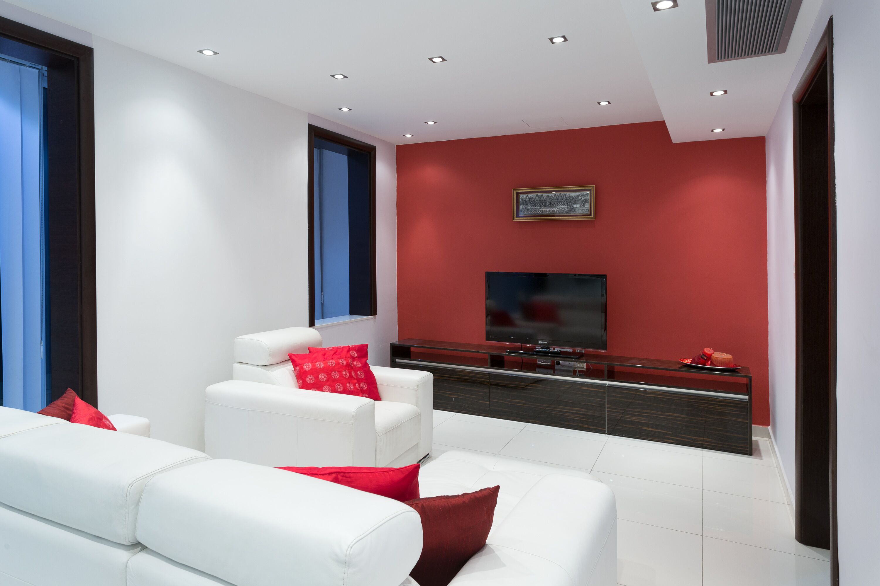 Uma sala de estar moderna com sofás brancos, uma parede de destaque vermelha e uma TV de tela plana.