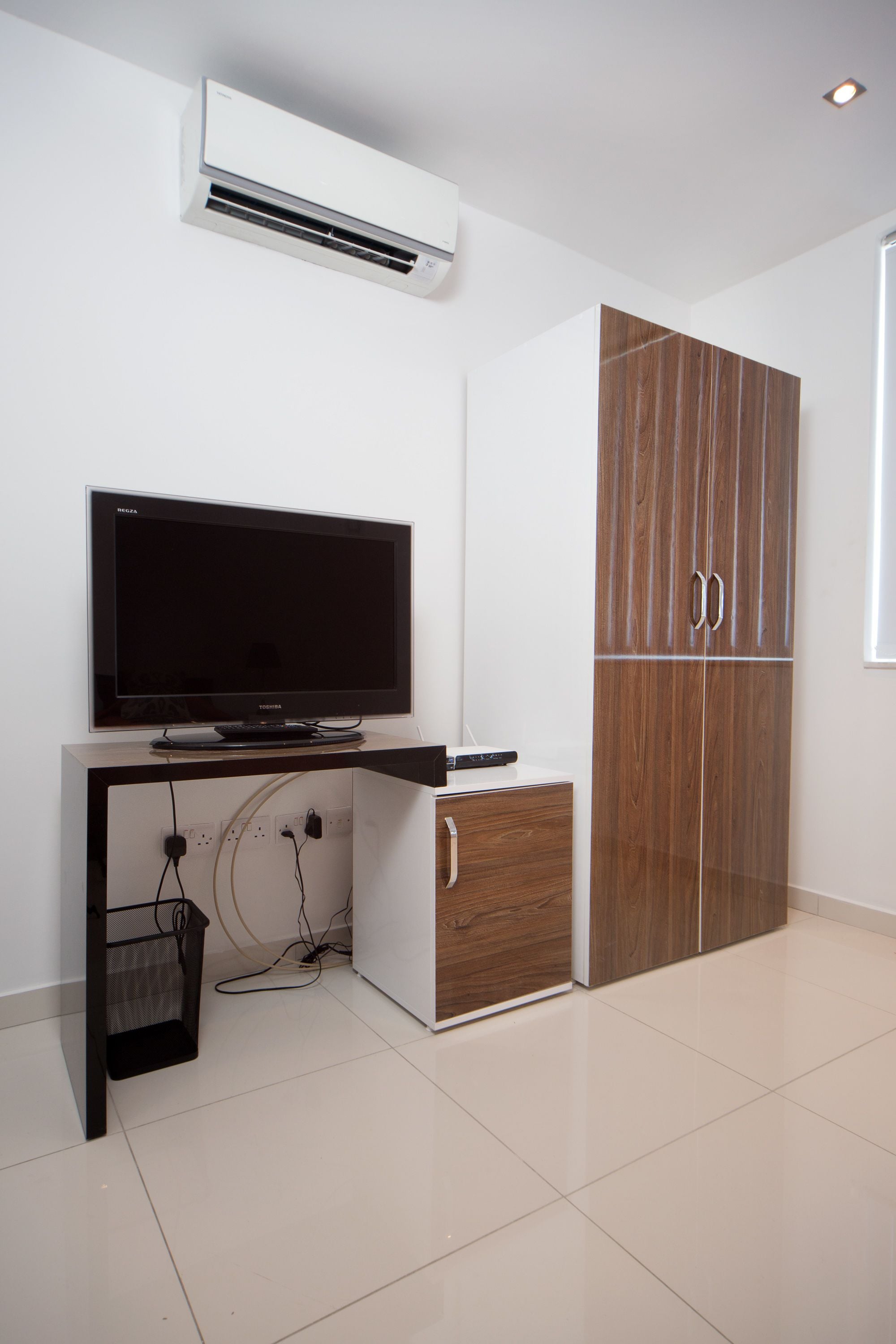 Een moderne kamer met een flatscreen televisie op een bureau, een garderobe met houten deuren en een airconditioner aan de muur.