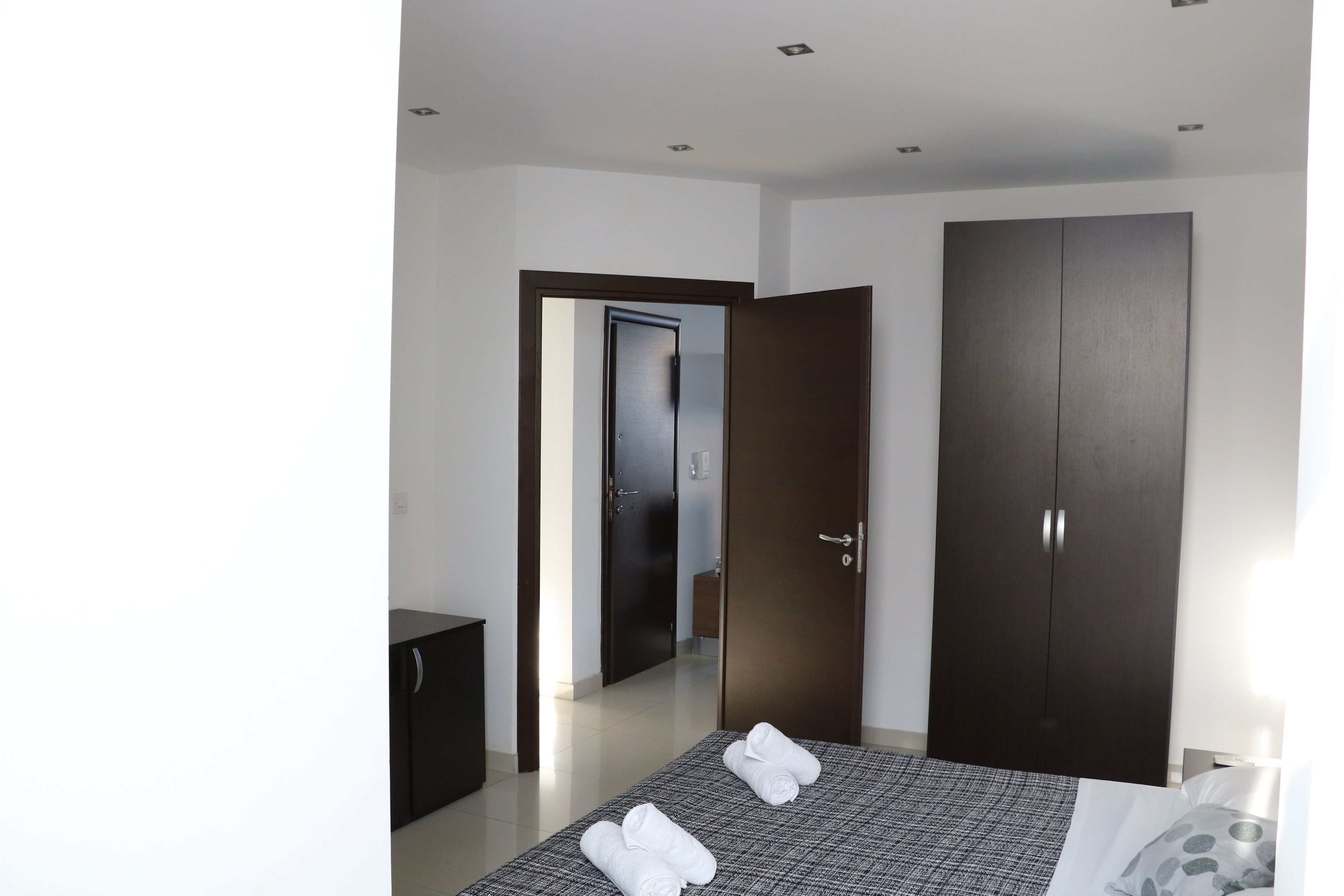 Ein modernes Hotelzimmer mit einem großen Bett, einem Kleiderschrank und einer Tür zu einem weiteren Raum.
