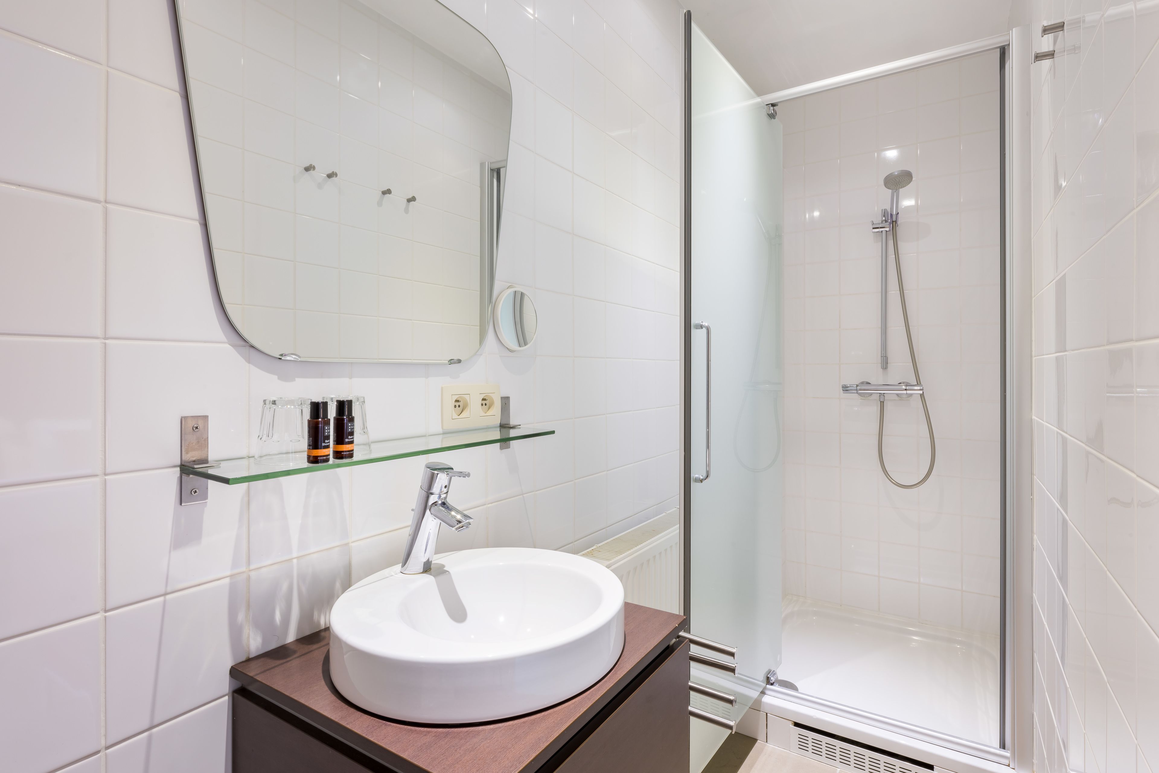 A modern bathroom with a white sink, glass shelf, and a glass-enclosed shower.
