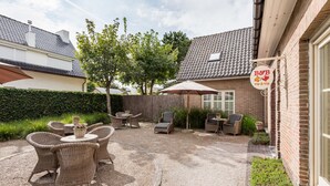 An outdoor patio area with wicker furniture, a gravel path, and a brick building with a sign. - B&B Vis-à-Vis (De Haan)