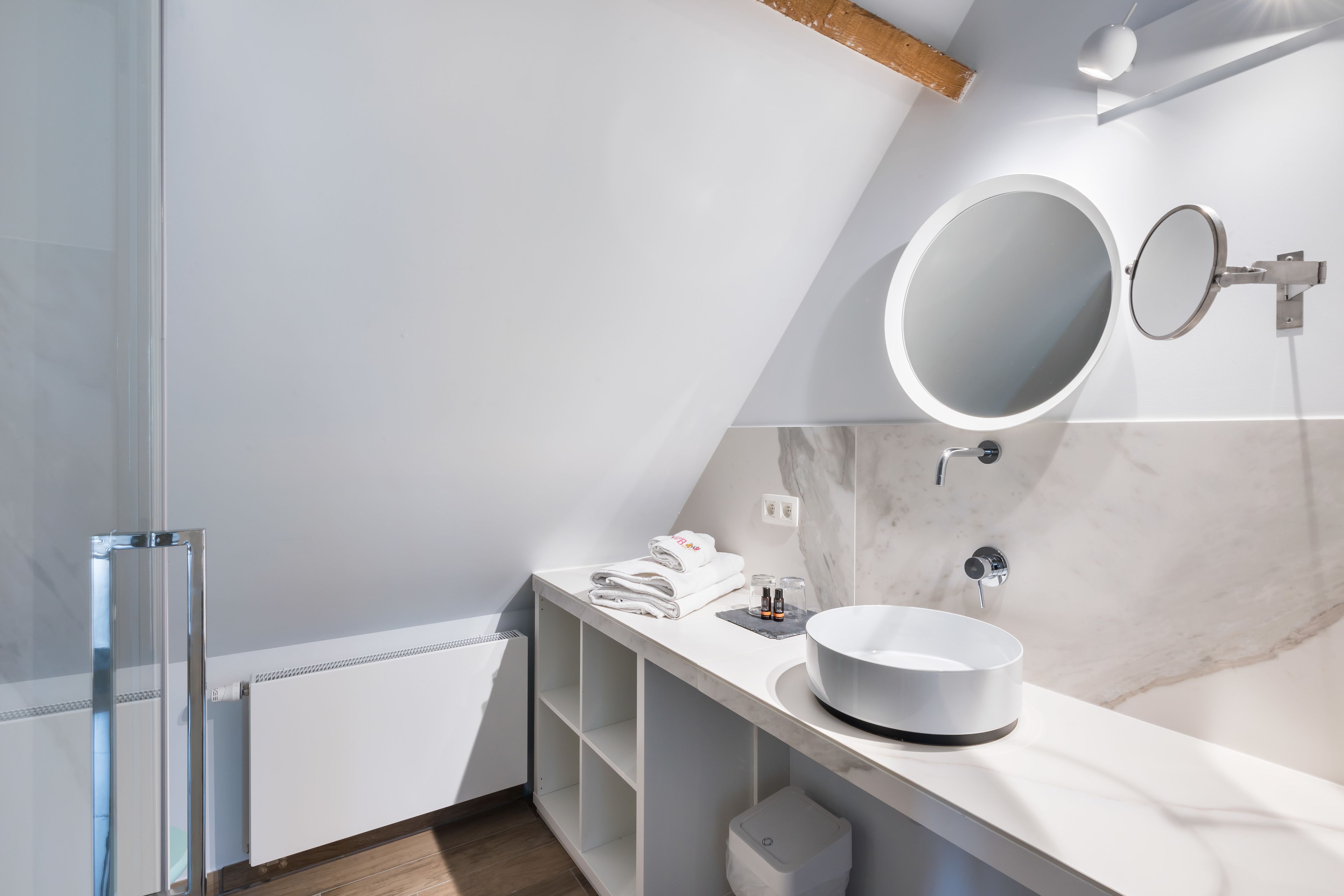 A modern bathroom with a large round mirror, a white sink, and a towel rack.