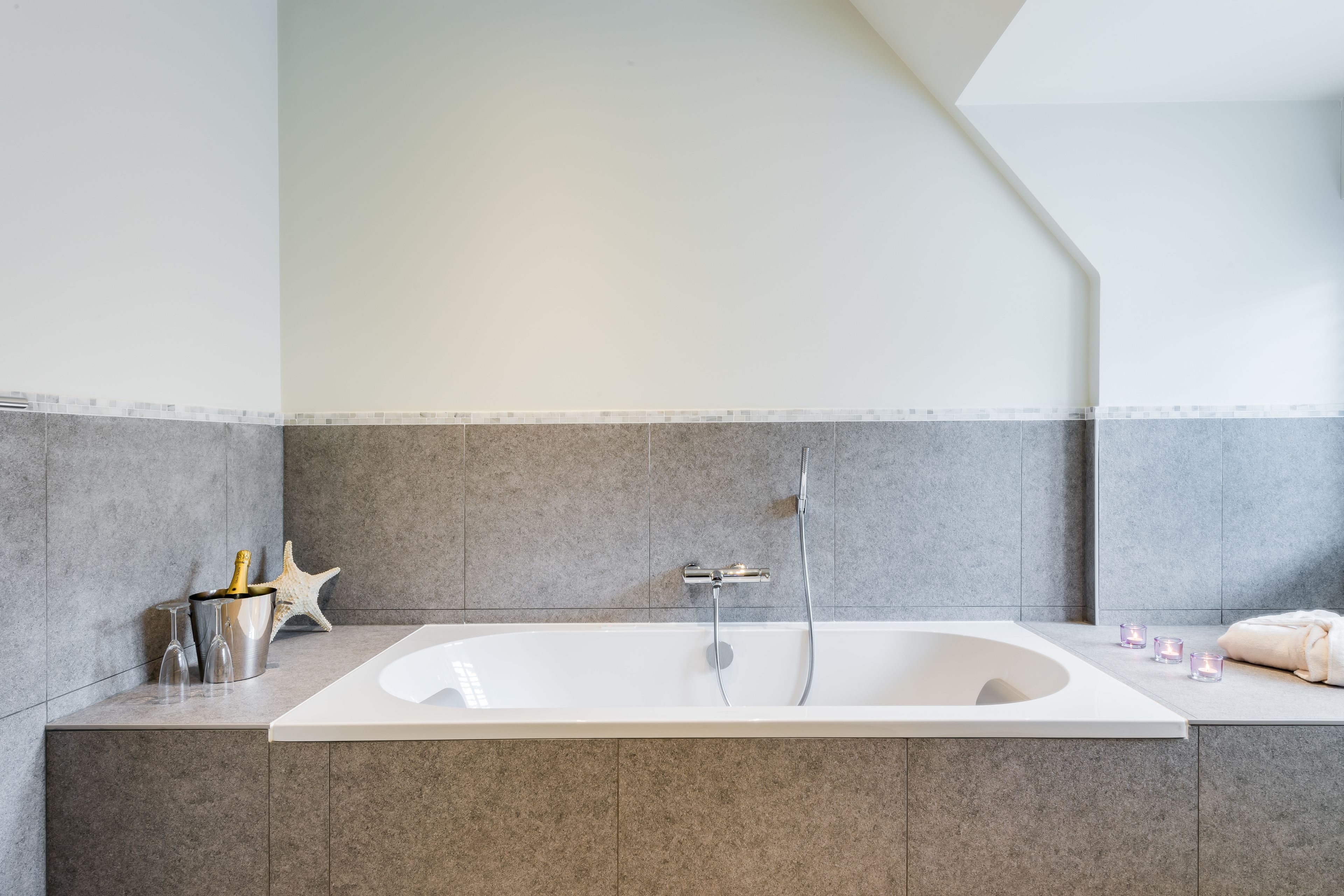 Een moderne badkamer met een groot bad, grijze tegels, een zeester decoratie en een handdoek op het aanrecht.