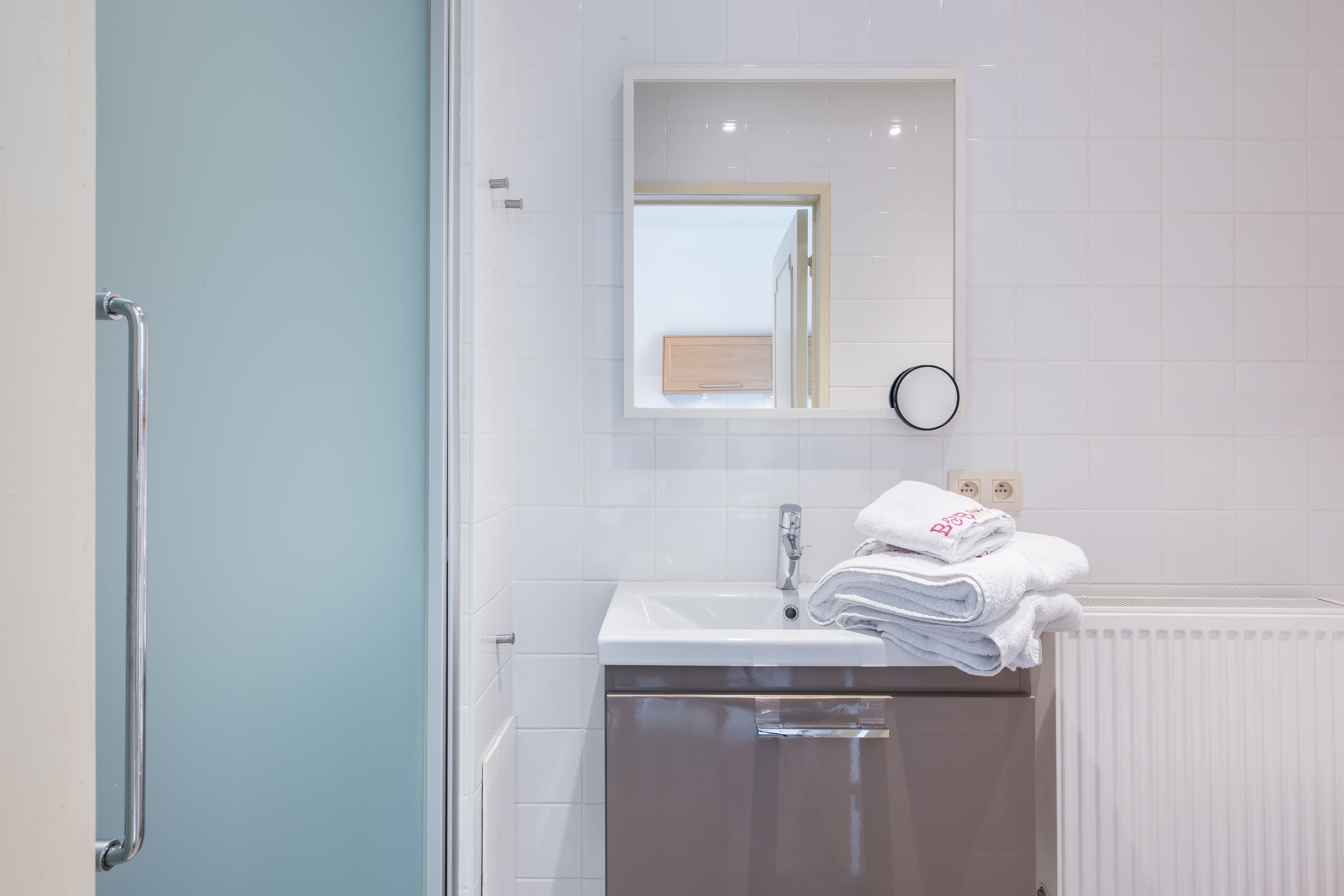 Een badkamer met een witte wastafel, een spiegel en een handdoekhouder.