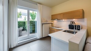 A modern kitchen with white cabinetry, a built-in oven, and a large window with curtains. - B&B Vis-à-Vis (De Haan)