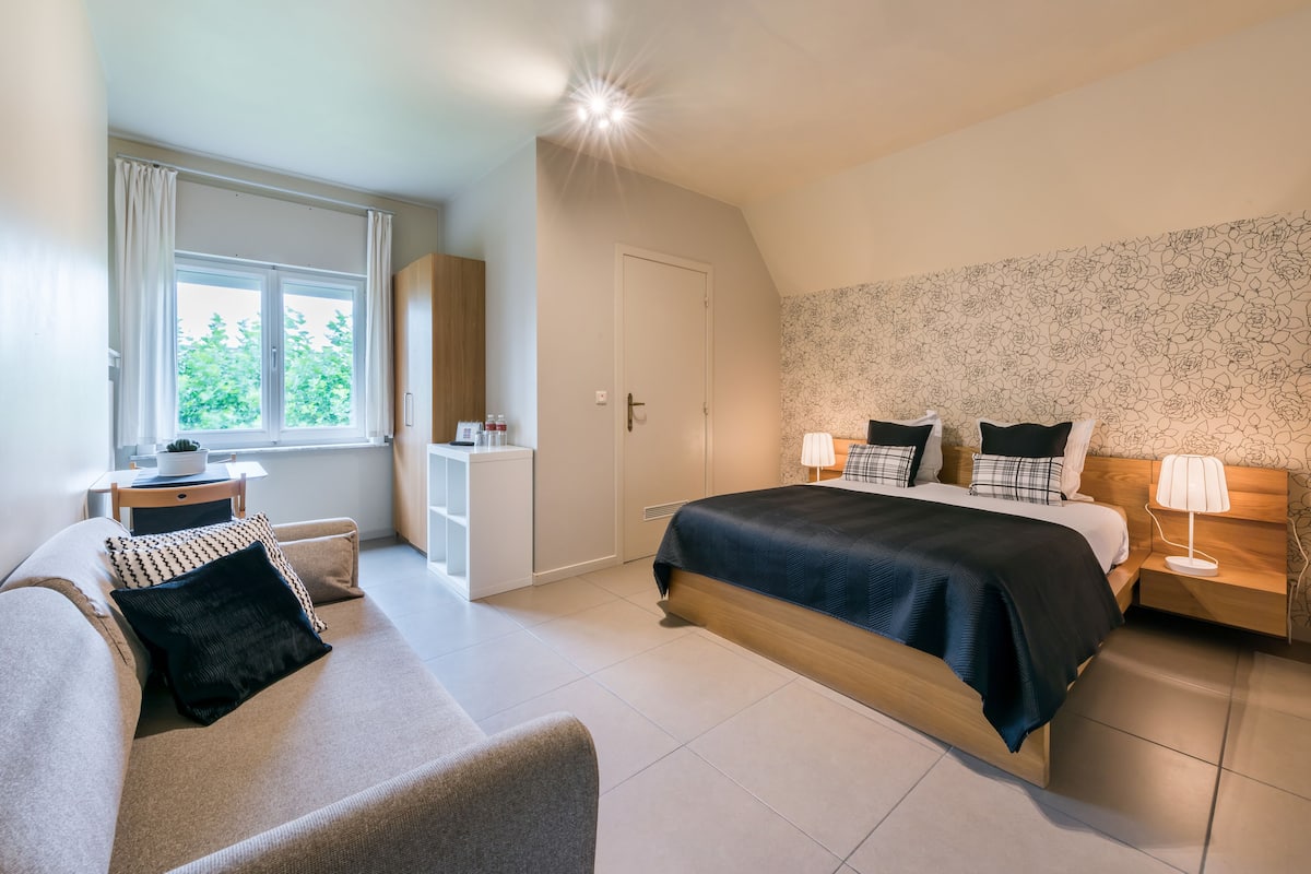 A modern bedroom with a bed, bedside tables, a sofa, and a window with curtains.