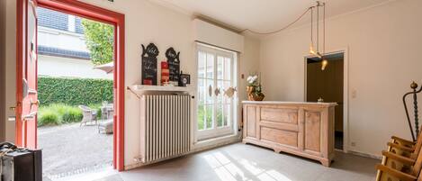 A hotel room with a red door, a radiator, a wooden cabinet, and a seating area with chairs.