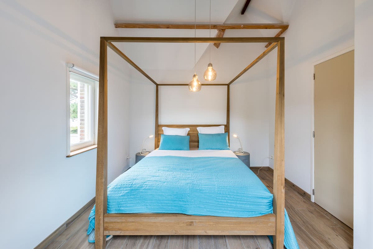 A four-poster bed with a wooden frame and a blue bedspread. There are two bedside tables with lamps.