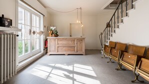 A spacious room with a large window, a wooden bench along the wall, and a central wooden cabinet. - B&B Vis-à-Vis (De Haan)