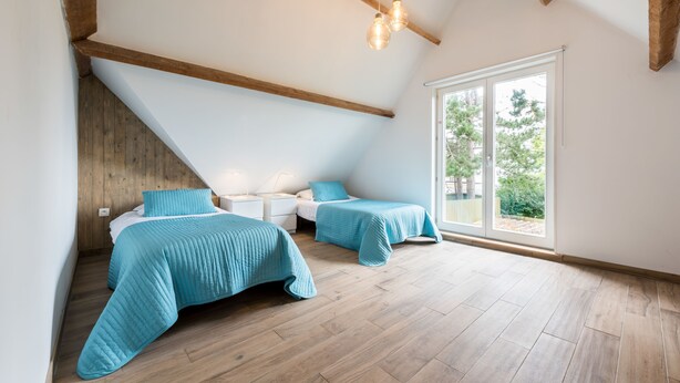 A bedroom with two beds, wooden beams, a large window, and a sloped ceiling. - B&B Vis-à-Vis (De Haan)