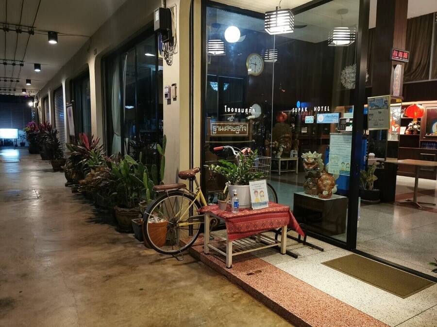 En hotelindgang med en cykel parkeret udenfor, et bord med et skilt og plantekasser langs stien.