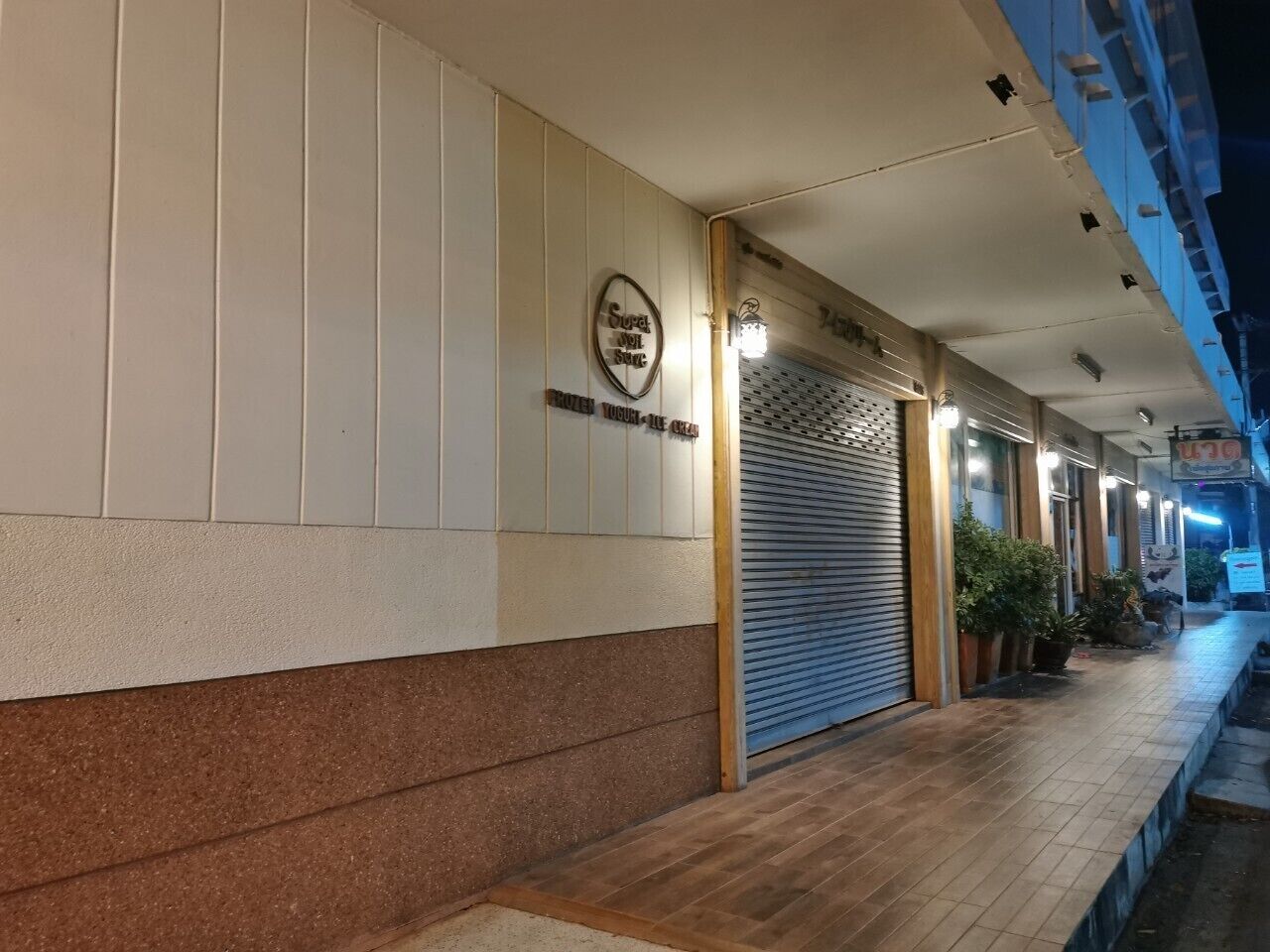 Ein Hotelkorridor mit heruntergelassenen Rollläden, einem Schild und Pflanzkübeln entlang des Weges.