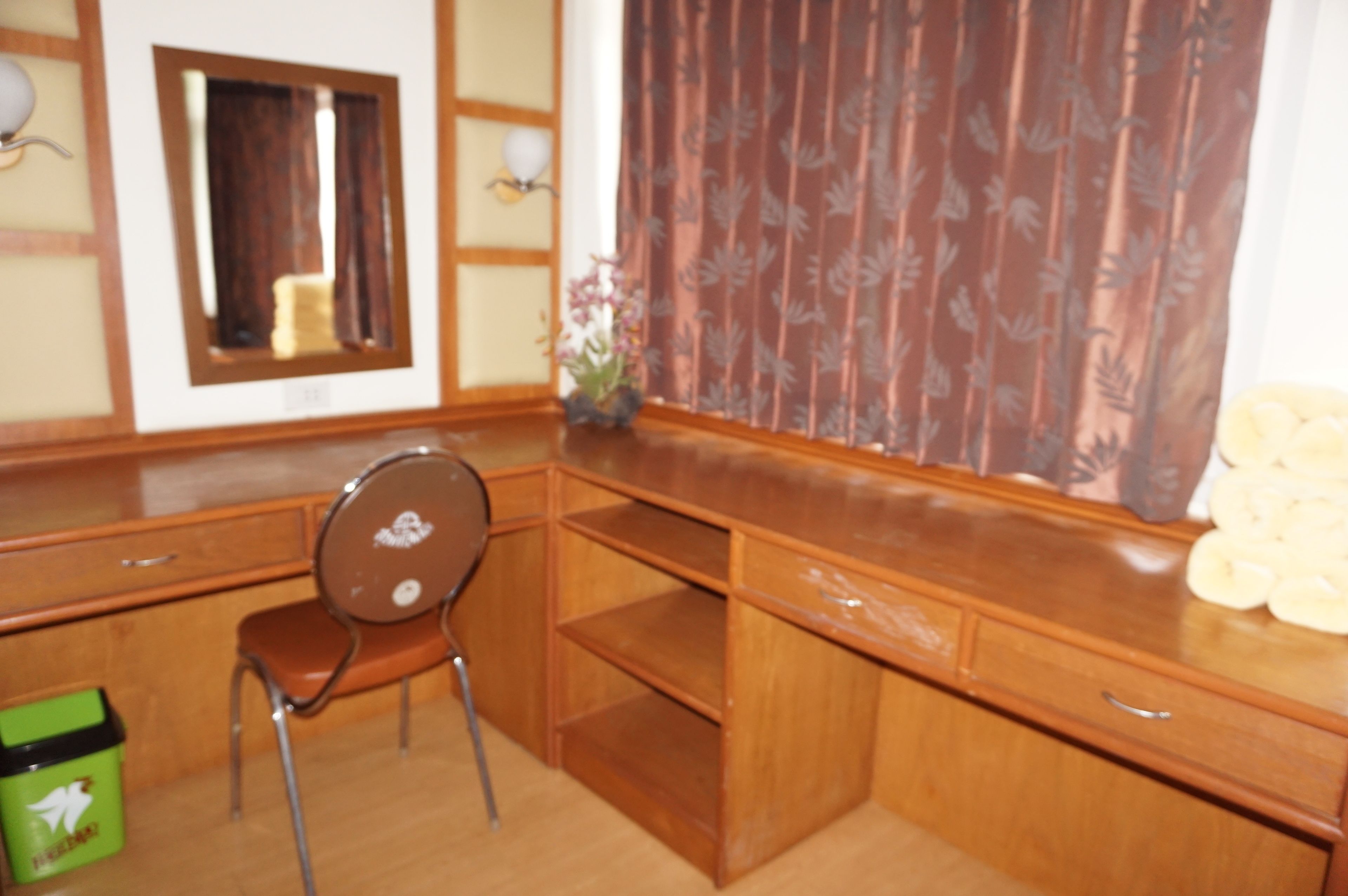 A wooden desk with a chair, a mirror, and a window with curtains.